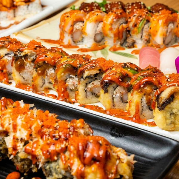 Assortment of sushi rolls with spicy sauce, fish roe, and nigiri, garnished with a purple orchid.
