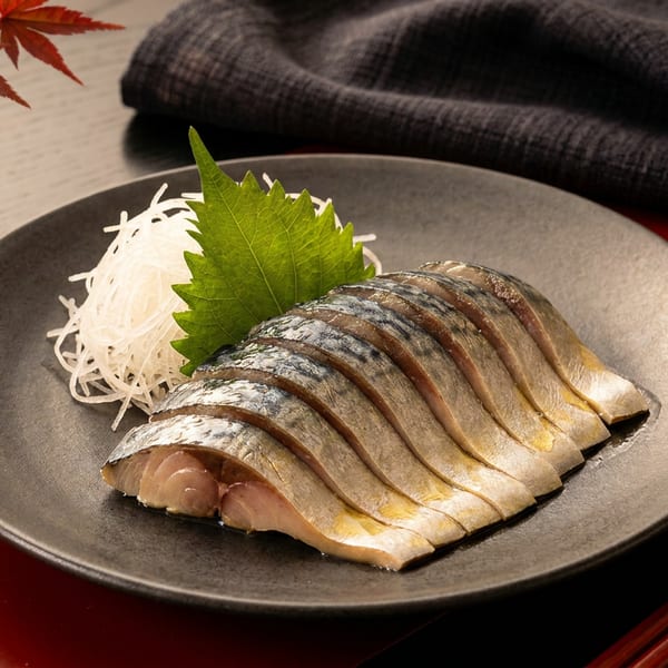 Japanese mackerel sashimi with shredded daikon and shiso leaf on a dark plate.